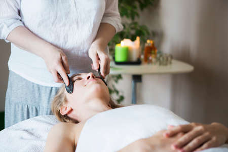 Young woman have face guasha treatment at asian beauty clinicの写真素材