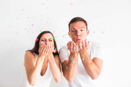 Young man and woman blowing confetti decorations on white backgroundの写真素材