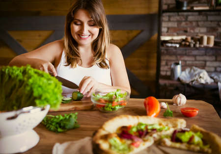 Young woman making vegetable salad at kitchenの写真素材