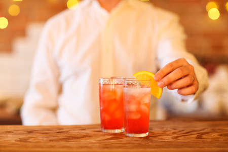 Bartender making two cocktails on wooden bar counter