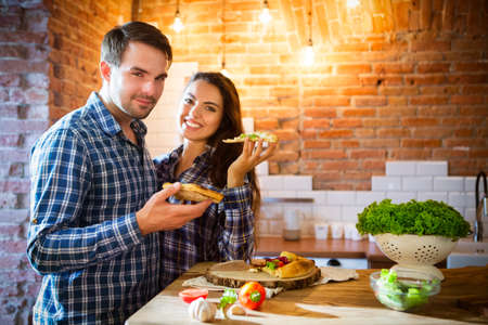 Young smiling couple eating homemade pizza together at kitchenの写真素材