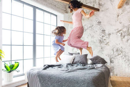 Family fun. Mother and daughter jumping on the bedの写真素材