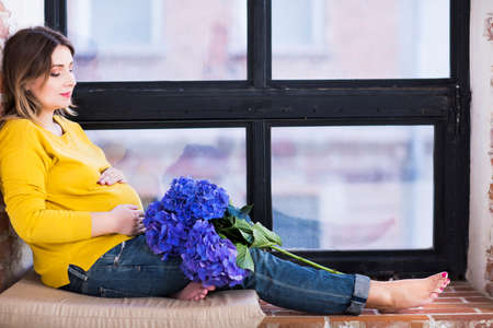 Pretty pregnant woman indoors sitting near windowの写真素材