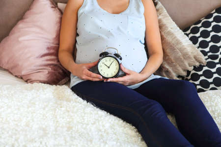 Pregnant woman indoors sitting on the bed. Concept. Time to birthの写真素材
