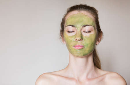 Beautiful relaxed woman having green clay face mask at homeの写真素材