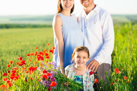 Portrait of a young big pregnant family in poppy field. Summer timeの写真素材