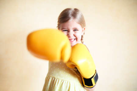 Little girl with yellow boxing gloves over yellow wall background. Girl power concept. Funny little kid portrait. Happy lost tooth little girl portraitの写真素材