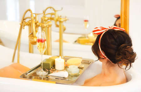 Attractive girl relaxing in bath with tray of cosmetics on light background の写真素材
