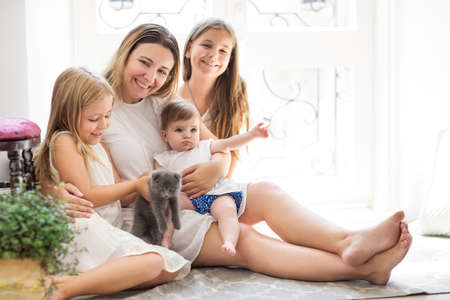 Young pretty woman and daughters playing with kitten indoors の写真素材