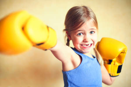 Little girl with yellow boxing gloves over yellow wall background. Girl power concept. Funny little kid portrait. Happy lost tooth little girl portraitの写真素材