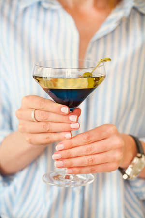 Woman holding glass with martini and green olives, focus on the glass