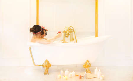 Attractive girl relaxing in bath with tchampgne on light background の写真素材