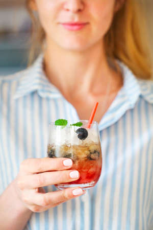 Woman holding blueberry cocktail with ice decorated by mint in her hand