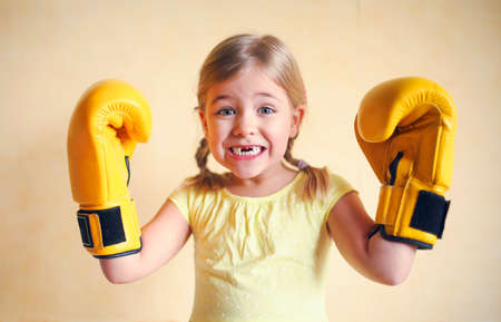 Little girl with yellow boxing gloves over yellow wall background. Girl power concept. Funny little kid portrait. Happy lost tooth little girl portraitの写真素材