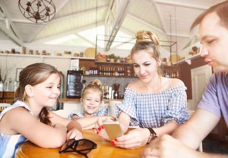  Happy family with two daughters having dinner and using smartphone at restaurant. Family, parenthood, technology concept.
の写真素材