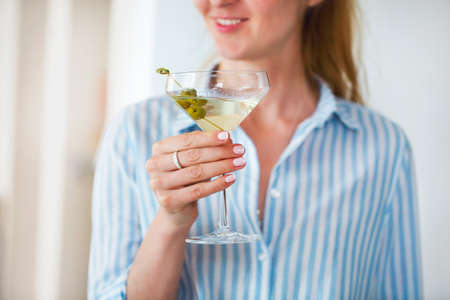 Woman holding glass with martini and green olives, focus on olives の写真素材
