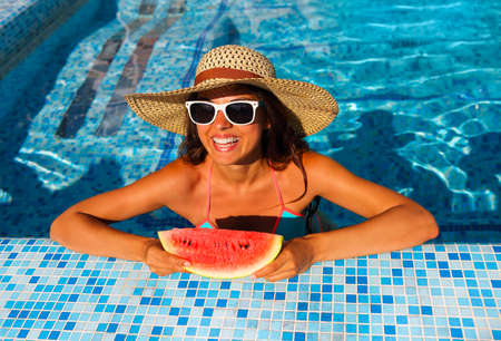 Sexy woman with dark hair eating watermelon in the pool