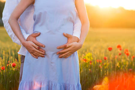 Young beautiful pregnant couple in poppy field. Close upの写真素材