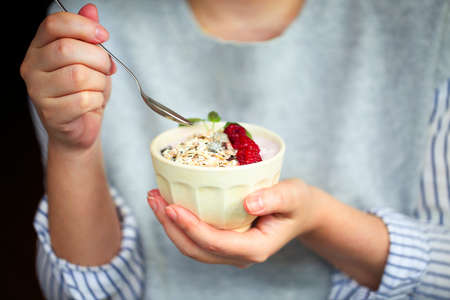 Healthy breakfast greek yogurt, granola and raspberries in the bowl in hands of woman の写真素材