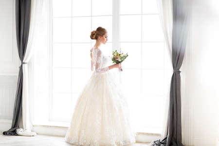Young beautiful blond woman with bouquet posing in a wedding dress の写真素材