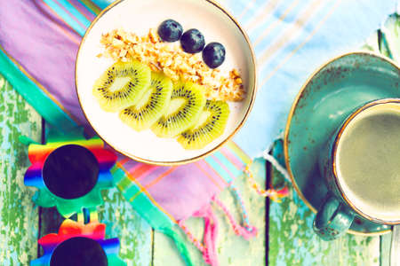 Cup of granola with yogurt and fruit on turquoise background