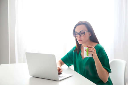 Young woman with computer and cup of coffee indoors