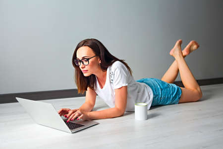 Young woman with computer and cup of coffee indoors