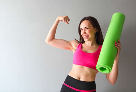 Attractive woman wearing pink sportswear holding green yoga or fitness mat after working out at home...