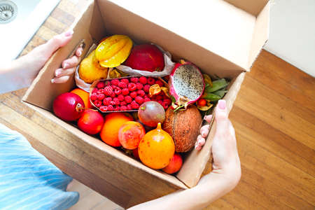 Young woman holding a box with fruits and vegetables in the home kitchen. Close up. Top view. Healthy life conceptの写真素材