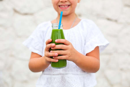 Little girl is drinking green fresh juice using straw outdoors. Close up