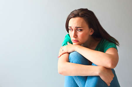 Portrait of a sad woman looking thoughtful about her troubles in front of a gray wall