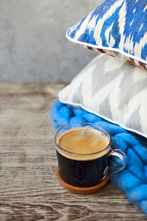 Blue and grey pillows with blanket and cup of coffee on the wooden background. Close up