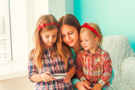 Three sisters looking at camera, sitting in big white armchair on blue wall looking cameraの写真素材