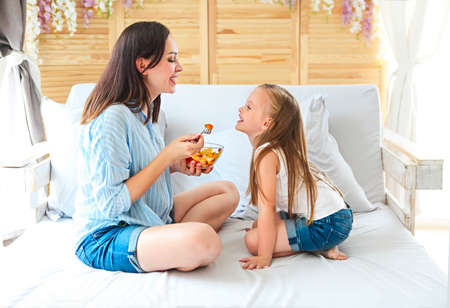 Mother and daughter sitting on bed at home having fruit salad for the breakfastの写真素材