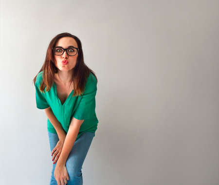 Young brunette woman by the grey wall smiling at the camera
