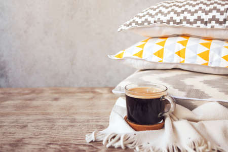 Yellow and grey pillows and cup of coffee on the wall background. Close up
