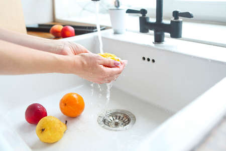 Woman washing fruits in the sink home kitchen. Close up