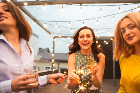 Group of partying girls with flutes with sparkling wine and bengal fire having fun on the partyの写真素材