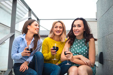 Three young happy woman laughing, drinking red wine, having fun. Party and friendship concept.の写真素材