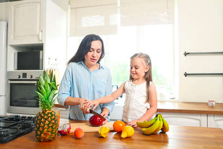Beautiful little girl with her mother in the kitchen preparing a fresh fruit saladの写真素材