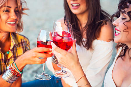 Happy female friends with glass of rose wine on summer beach picnicの写真素材