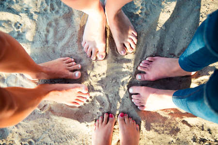 Top view image of feet of the female friends standing on the sand beach