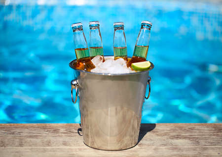 Closeup view of bucket with ice cubes, beer bottles and lime slices by the pool