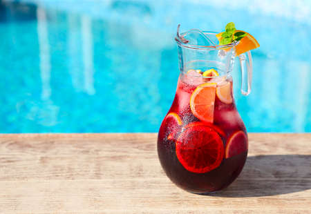 Glass jug of iced sangria with strawberry, orange, apple and lemon by the poolの写真素材