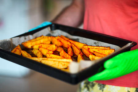 Close up shot of roast potatoes and parsnips in a tray. A man is holding it in his hands wearing...