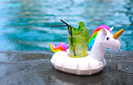 Mojito cocktail at the edge of a resort pool in inflatable unicorn. Concept of luxury vacation. Outdoor pool backgroundの写真素材