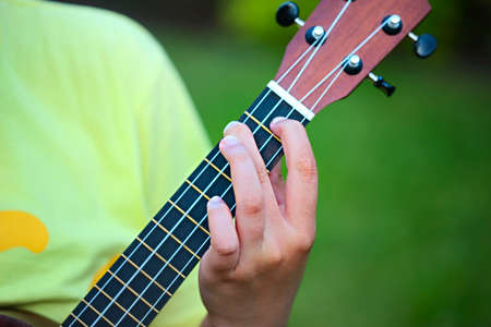 Cute teen girl playing her ukulele outdoors in the evening. Close up
