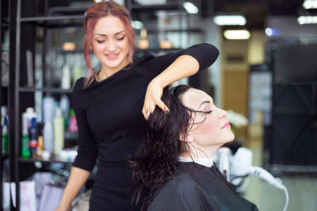 Professional hairstylist drying hair of the beautiful young woman at the beauty studio. Professional beauty care conceptの写真素材