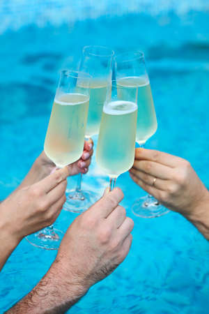 People hold champagne glasses in the pool. Summer pool party