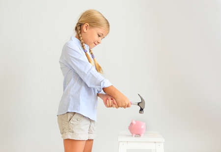 Little girl with hammer by the pink pig piggy bank on a white backgroundの写真素材